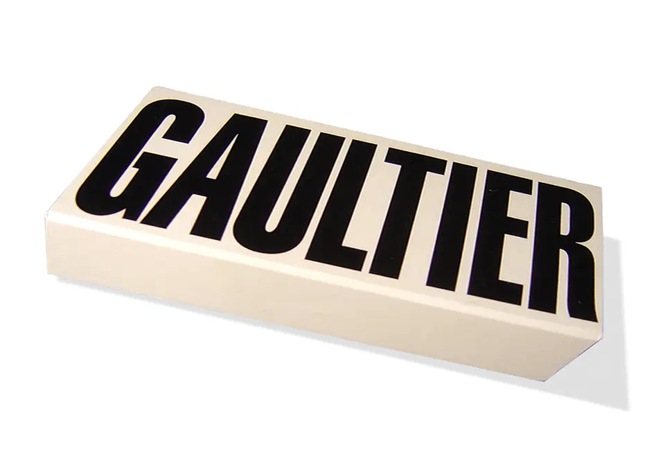 Gaultier - Coffret avec couvercle à rabat aimanté contrecollé rembordé d’un papier couché – impression d’un aplat – pelliculage mat – magnets sérigraphiés en PVC magnétique (plaque d’acier collée à l’intérieur du couvercle) – marquage à chaud au R° du couvercle – fermeture aimantée – poignée moulée – 2 grilles de calage superposées contrecollées de papier imprimé et pelliculé – rubans extracteurs et limiteur d’angle d’ouverture.